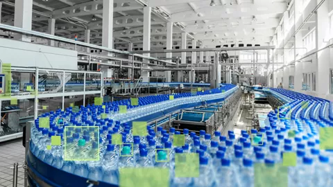 A view of filled plastic water bottles with dark blue caps on a conveyor in a bottling facility. Yellow square outlines are shown over bottles with teal caps, representing a computer vision system that alerts on product discrepancies