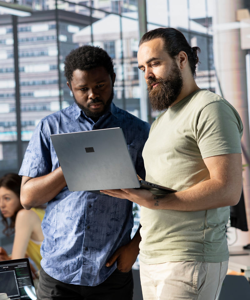 Two coworkers reviewing content together on a laptop in a modern office.