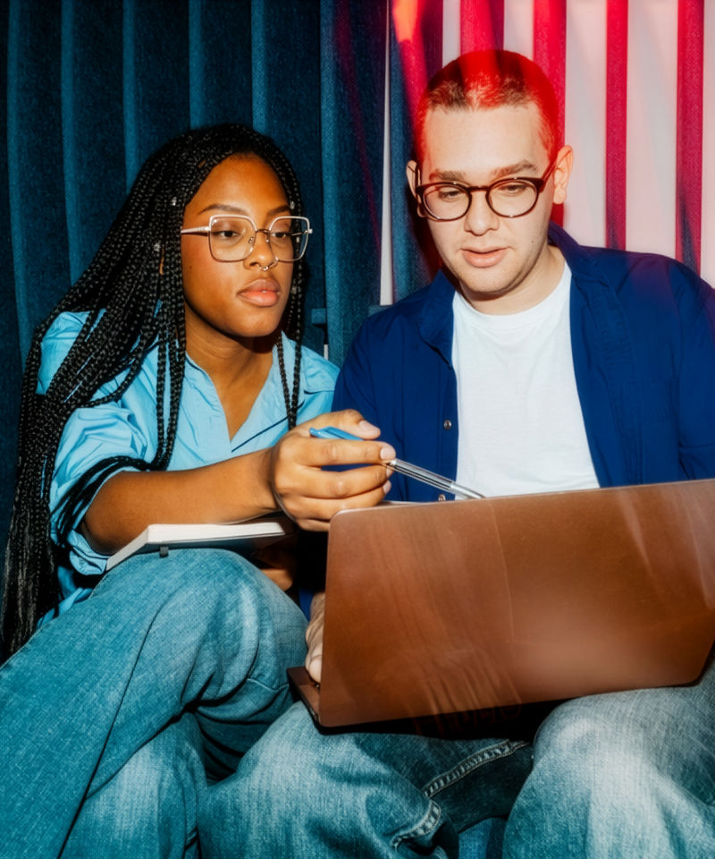 Female business professional assisting male colleague using laptop at office
