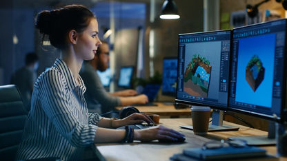 A professional works at a desktop PC with two monitors in a modern, open office environment