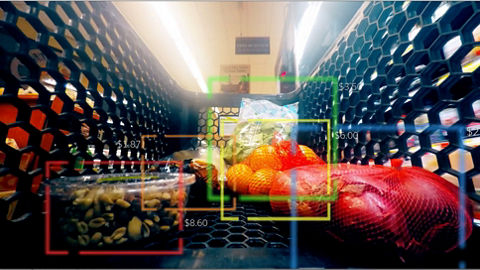 A close-up view of the inside of a grocery store shopping cart containing various food items. Colored outlines are shown around each item, representing computer vision identification windows