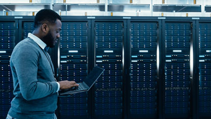 IT-Techniker im Rechenzentrum geht mit Laptop durch den Server-Rack-Flur.