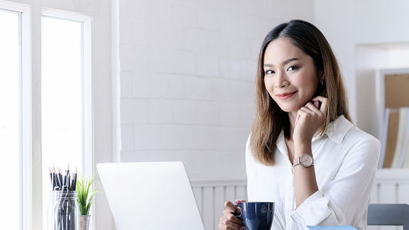 Female using a laptop while holding a cup.