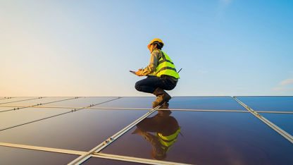 A worker in safety gear crouches on a solar panel.