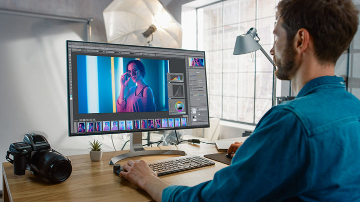 Eine Fotografin sitzt an einem Schreibtisch und passt Bildfarbe und Schattierungsdetails mit einem Desktop-Computer an