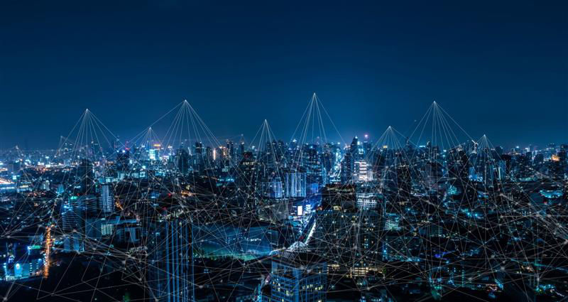 Horizonte urbano nocturno con edificios iluminados y líneas de red superpuestas.