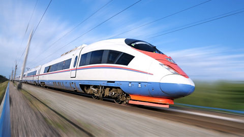 Modern-looking passenger train rapidly moving along rail tracks next to agricultural landscape