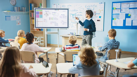 Schüler steht vor interaktivem Flachbildschirm und teilt Inhalte mit der Klasse