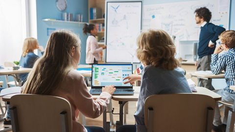 Two students in a classroom collaboratively review a flowchart on the same laptop.