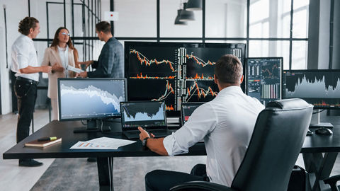 Un analyste est assis à un bureau devant plusieurs PC portables et grands écrans et est en train de passer en revue différents graphiques de tendances
