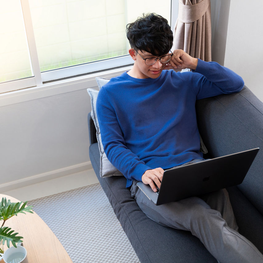 A man relaxes on a couch while working on a laptop