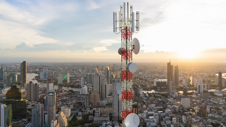 A bird’s-eye view of a communications tower with a cityscape at daybreak in the distance