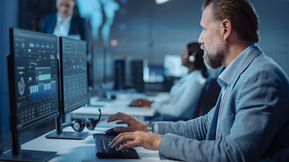 Controlador técnico profissional concentrado sentado à sua mesa com vários monitores de computador diante dele