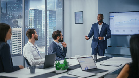 オフィス環境でノートブック PC の画面上の情報を見ている 2 人の同僚のクローズアップ写真。1 人はデスクに座り、もう 1 人が側に立ってデスクに身を乗り出し、片手でキーボードに入力している