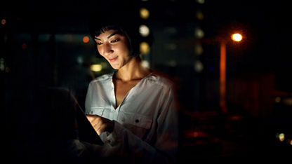A woman, smiling with her face illuminated by a tablet at night.