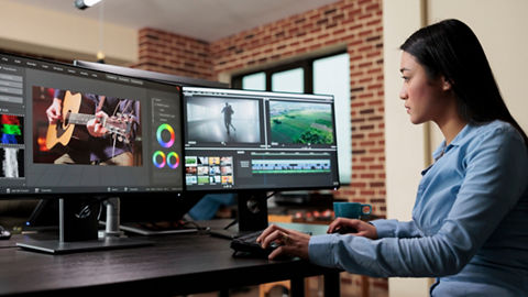 Content creator sitting at desk in front of two monitors editing video content