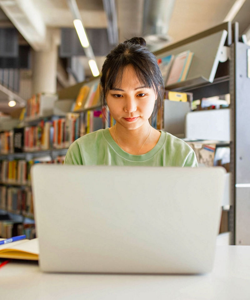 Young adult asian woman at the library studying and using her laptop