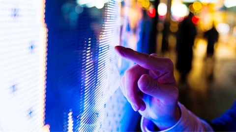 Man's finger pointing at LED screen of stock market price at night