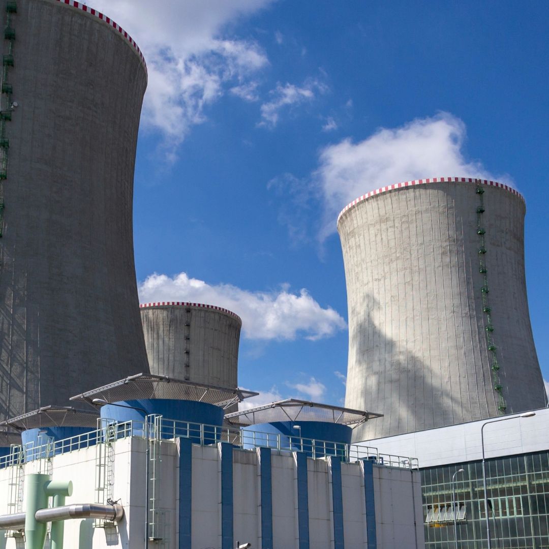 Three large cooling towers at a power generation facility against an open sky.