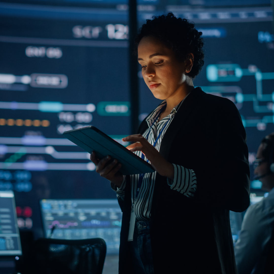 Person in professional attire working on a tablet in a server room.