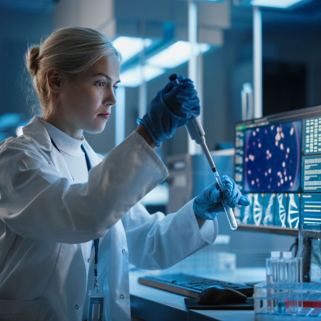 Person in a lab coat using a pipette next to a monitor displaying scientific data visualizations.