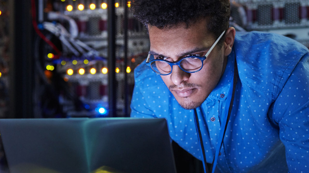 Man with glasses working on laptop in server farm