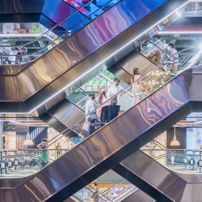 People riding escalators inside a brightly lit shopping mall
