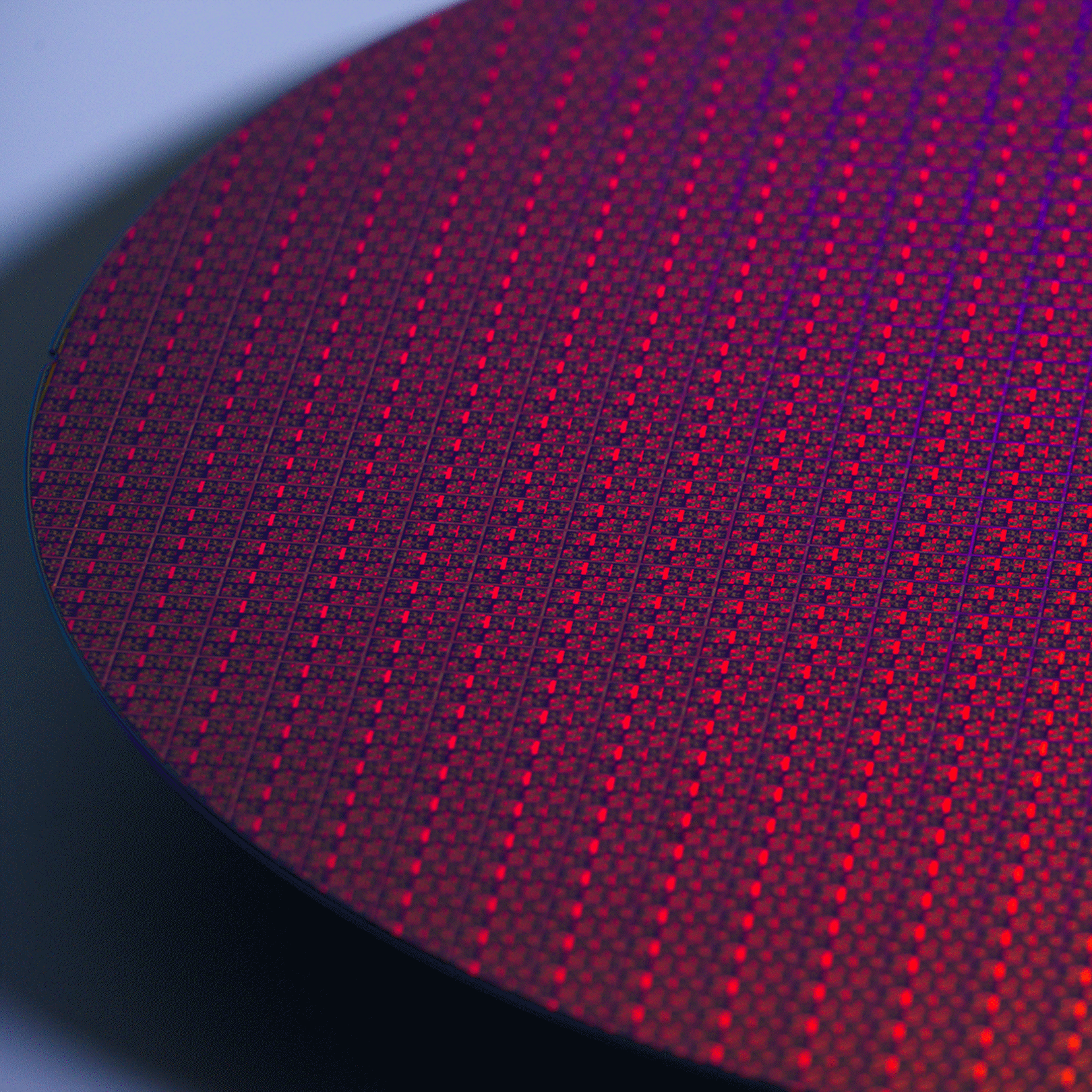 Close-up of a circular semiconductor wafer with red, orange and purple reflections.