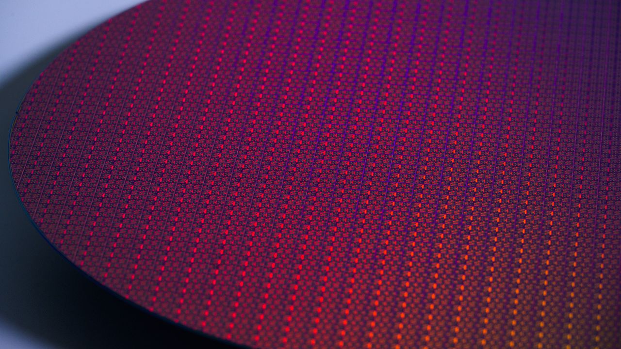 Close-up of a circular semiconductor wafer with red, orange and purple reflections.