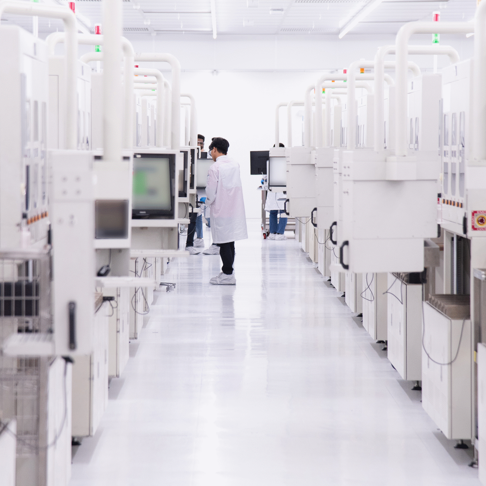 A person in a white lab coat works among rows of equipment in a bright Intel assembly and packaging facility in Malaysia.