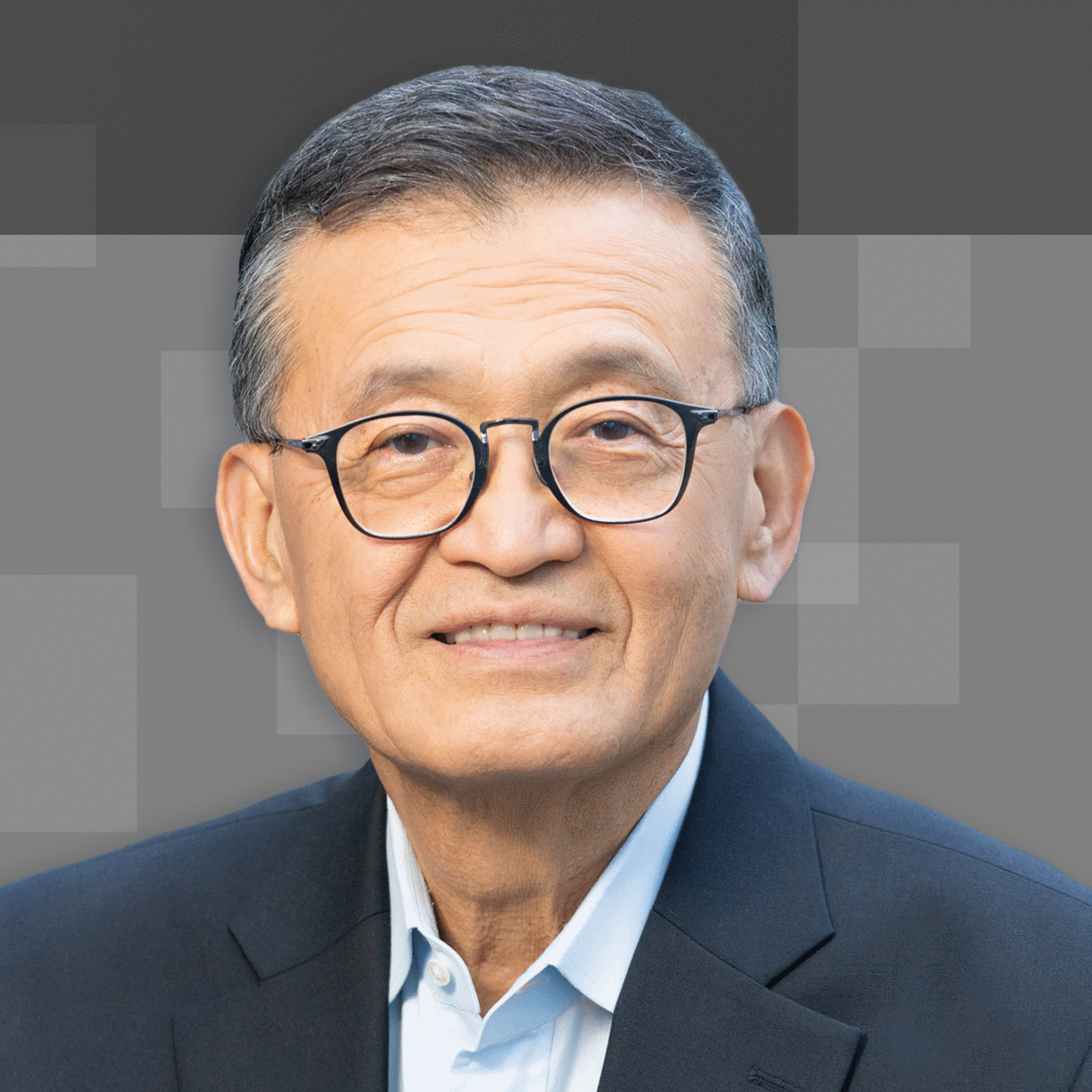 A smiling man with glasses and short hair wearing a dark suit and white shirt, set against a gray background with pixelated squares.