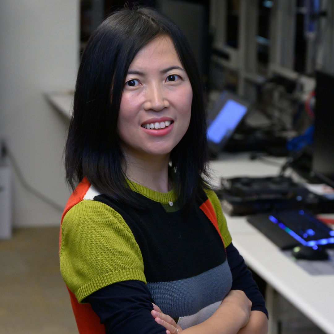 Dr. Olena Zhu standing in a computer lab surrounded by monitors and equipment.
