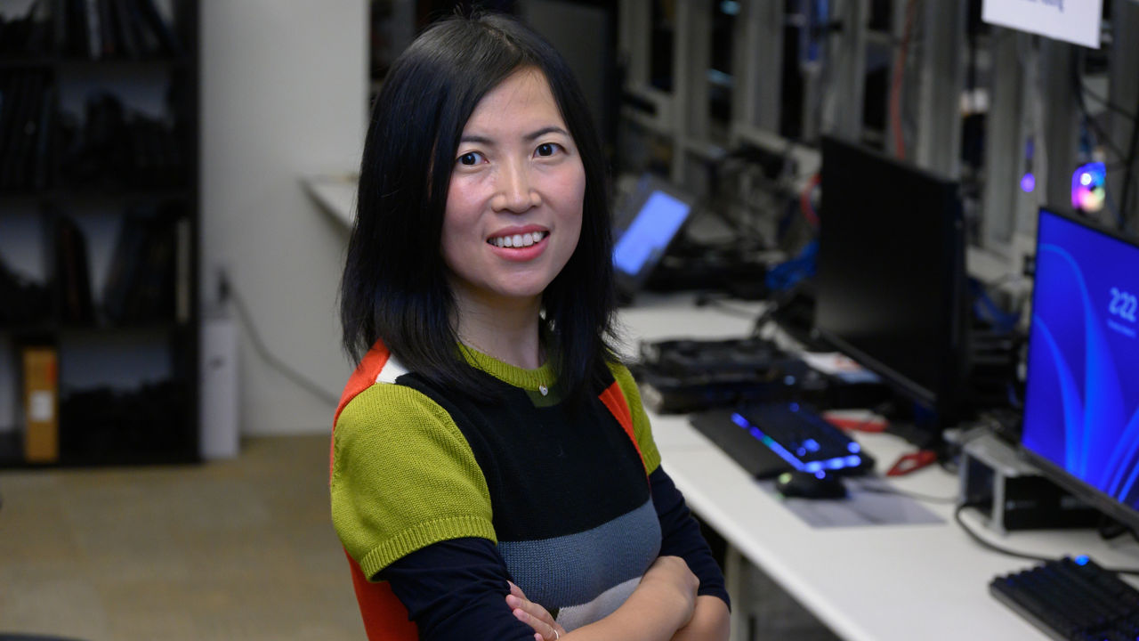 Dr. Olena Zhu standing in a computer lab surrounded by monitors and equipment.