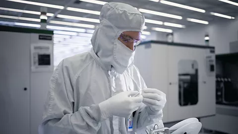 Person in cleanroom suit at manufacturing facility holding a tweezer