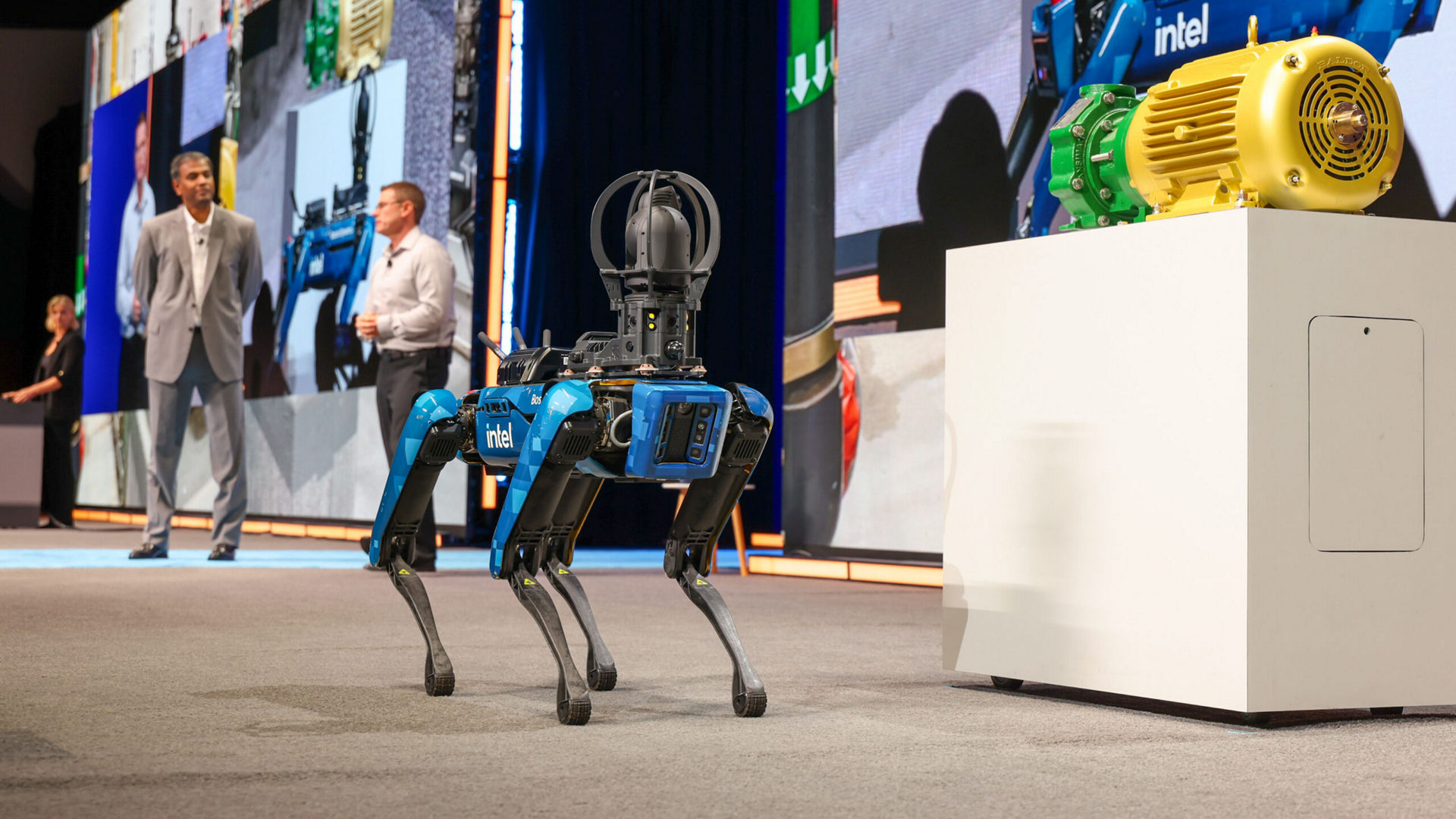 Intel's 'Chip' robot stands on stage next to industrial equipment during a keynote event.