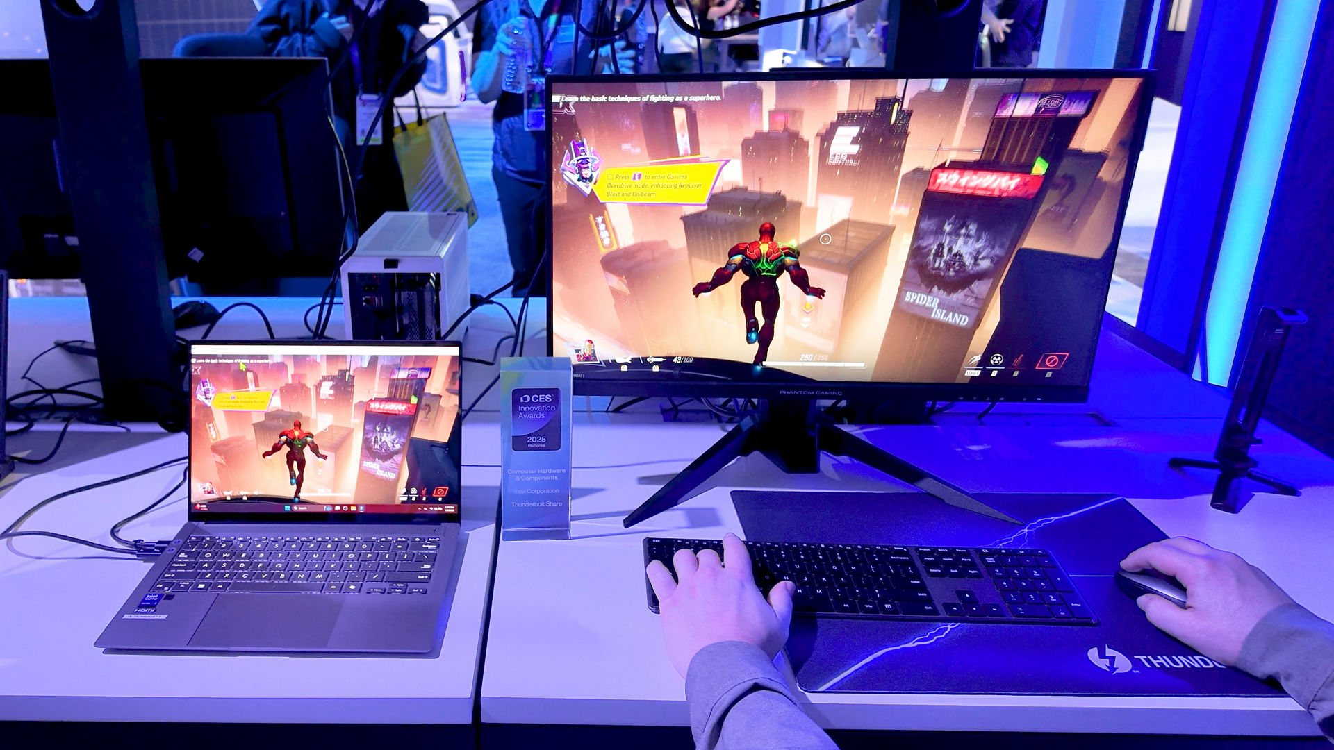 Uma pessoa joga num monitor de secretária, com o mesmo jogo apresentado num portátil ao lado.