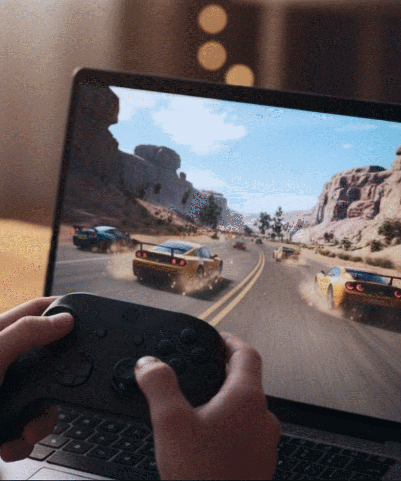 Person's hands using a controller to play a car racing game on a laptop