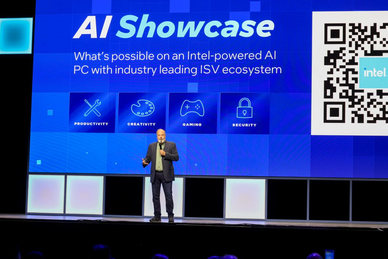 A speaker stands on stage in front of a large screen displaying AI Showcase with icons labeled Productivity, Creativity, Gaming, and Security. A QR code and an Intel logo are also visible on the screen.