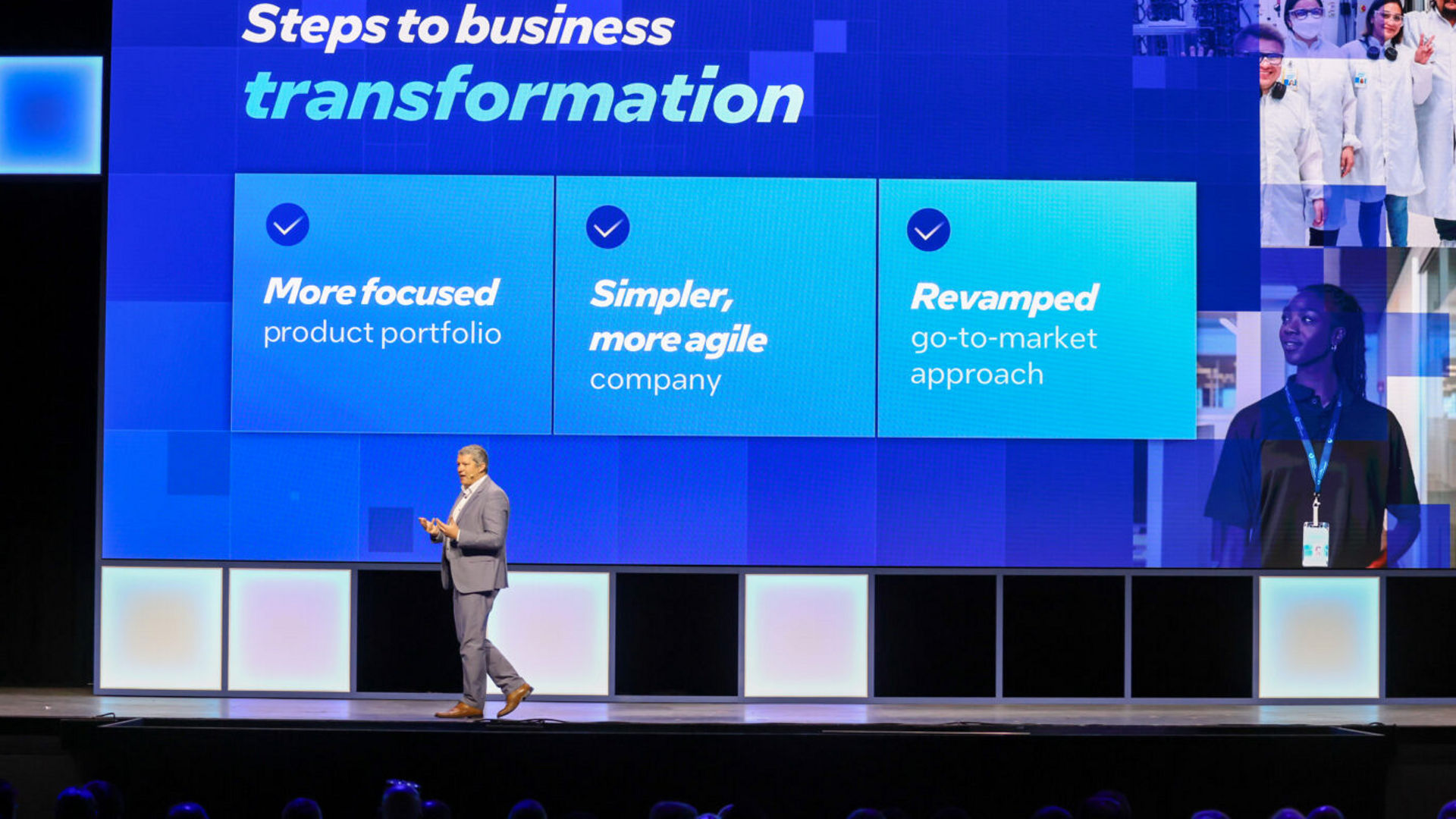 A person in business attire stands on stage, presenting a slide titled Steps to business transformation. The slide lists three points: More focused product portfolio, Simpler, more agile company, and Revamped go-to-market approach.