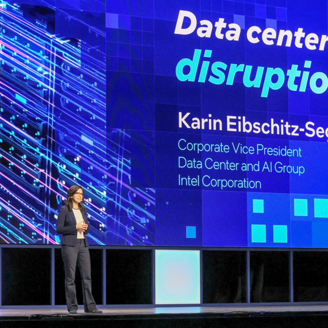A person is standing on a stage presenting. The large screen behind them displays the text Data center disruption and Karin Eibschitz-Segal, Corporate Vice President, Data Center and AI Group, Intel Corporation.