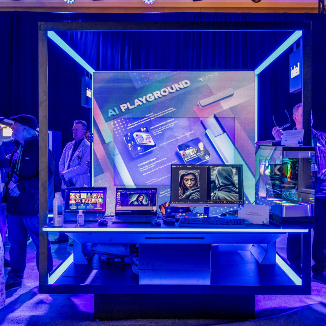 A tech exhibit labeled AI Playground features screens displaying digital graphics. Surrounded by blue lighting, attendees observe and interact with the setup. The atmosphere is vibrant and futuristic.
