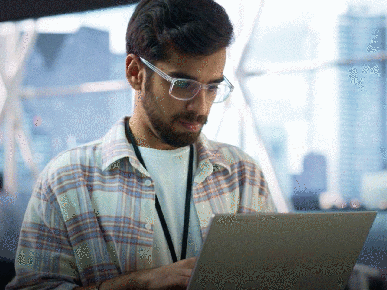 Man wearing a lanyard holding a laptop and looking intent