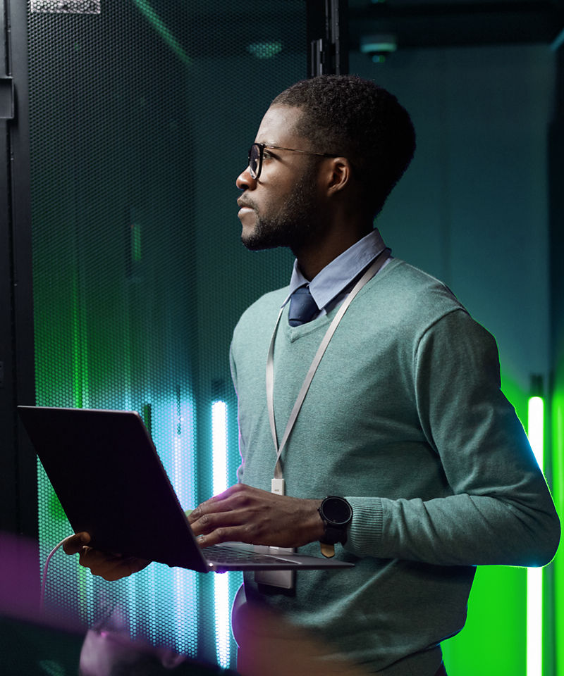 Uma pessoa em um data center, olhando para servidores e segurando um notebook.