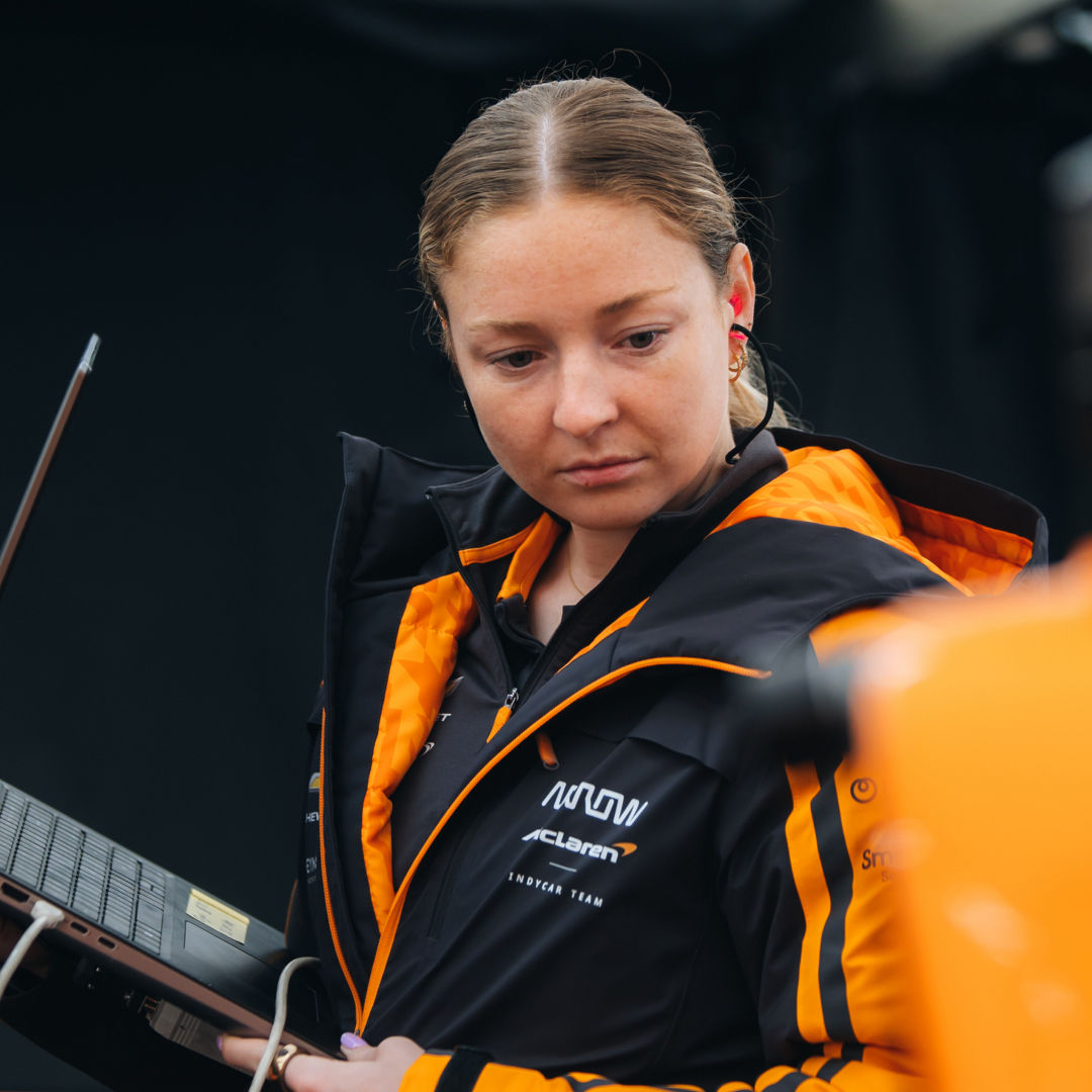 Image of a McLaren crew member working on a laptop with a headset on