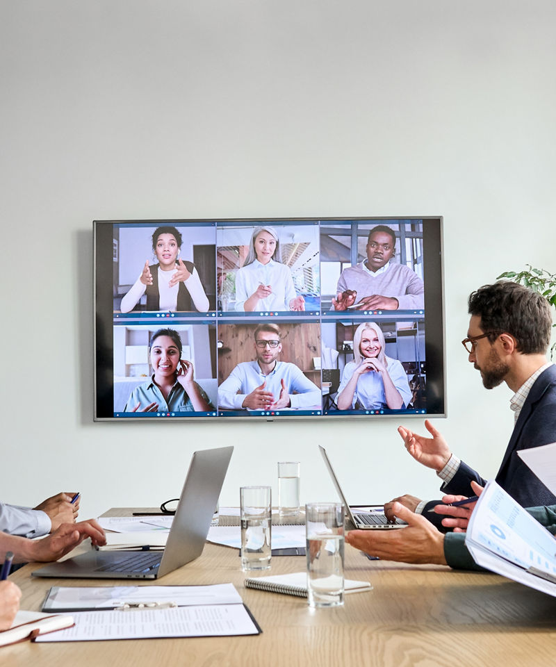 Multiple workers together at a meeting, in person and on screen.