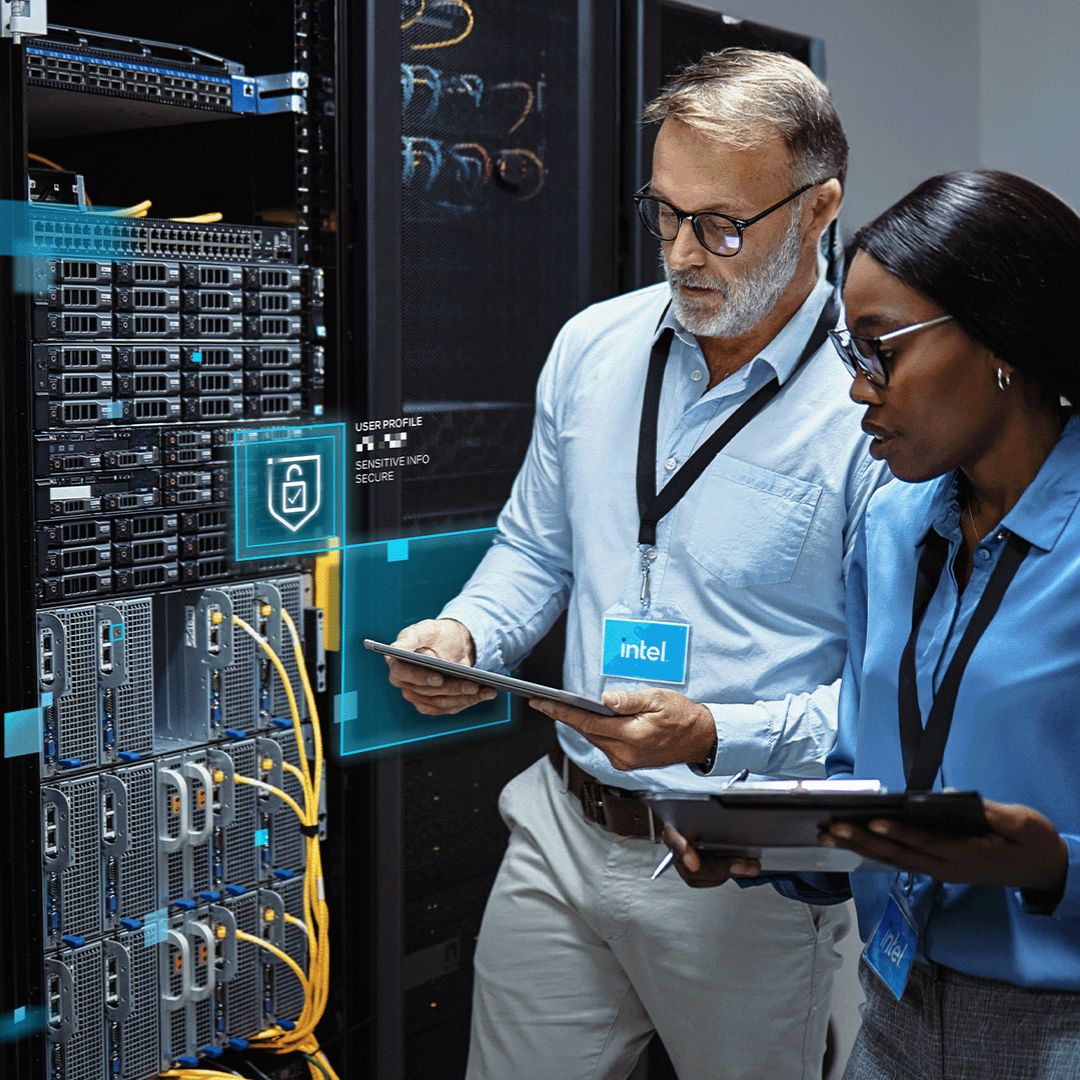 Two technicians standing in a data center, reviewing a tablet beside rows of server racks with status lights and cabling.