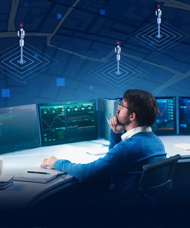 Person at a workstation in a network operations center showing telecommunications maps and system monitoring dashboards.